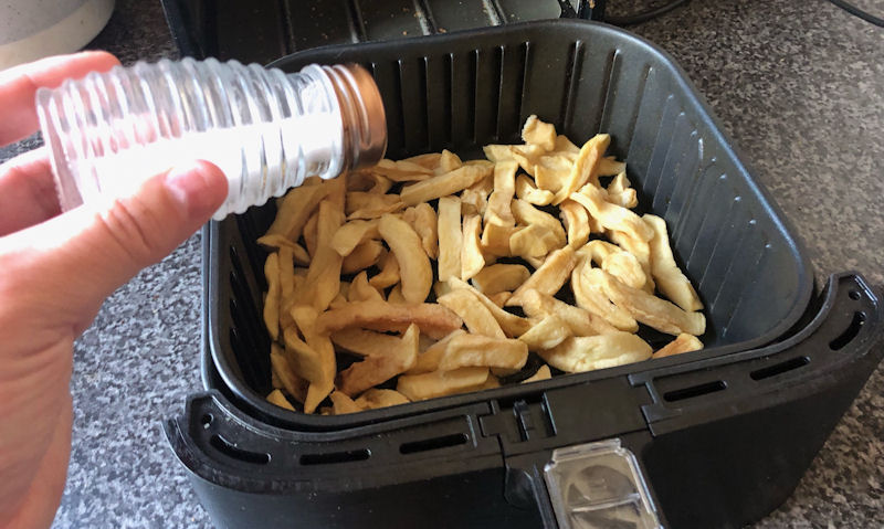 Shaking salt onto portion of chips sitting in air fryer basket