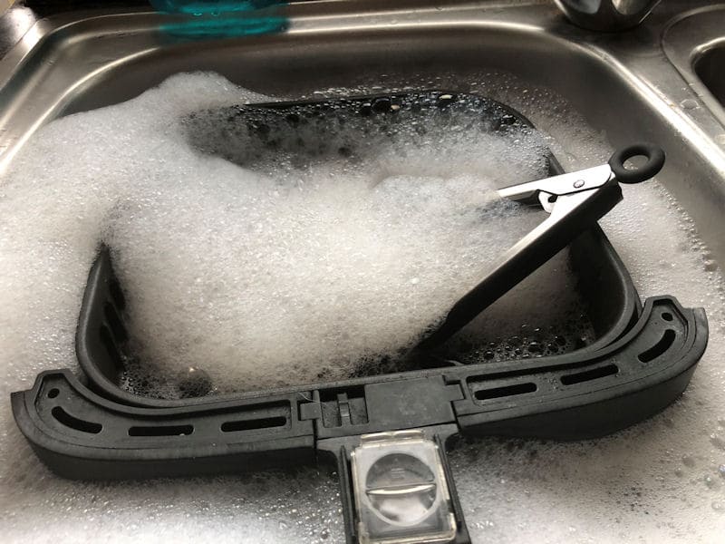 Air fryer basket and silicone tongs soaking in kitchen sink