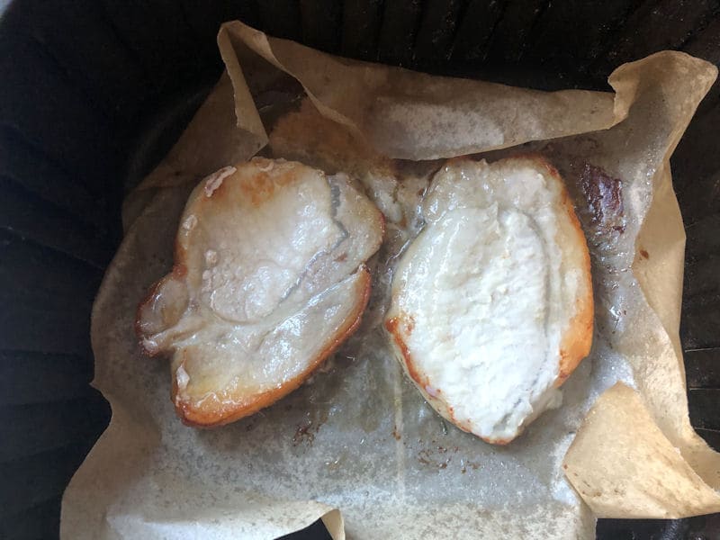 Air fried pork loin steaks on parchment paper in air fryer basket