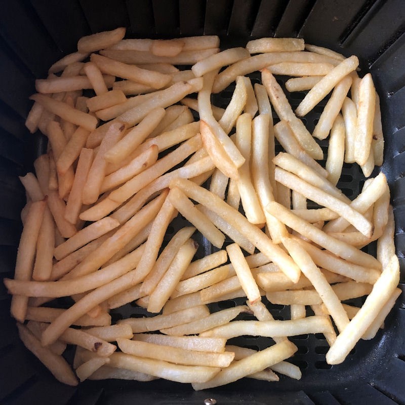 Pile of French fries scattered in air fryer basket