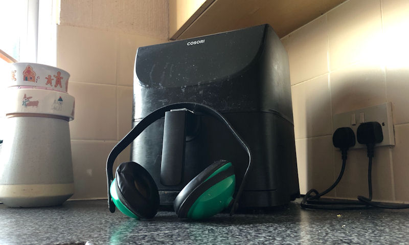 My Cosori air fryer sitting on kitchen countertop, ear protectors leaning on handle