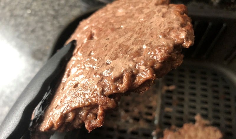 Close up shot of fully cooked air fried beef patty held in silicone tipped tongs