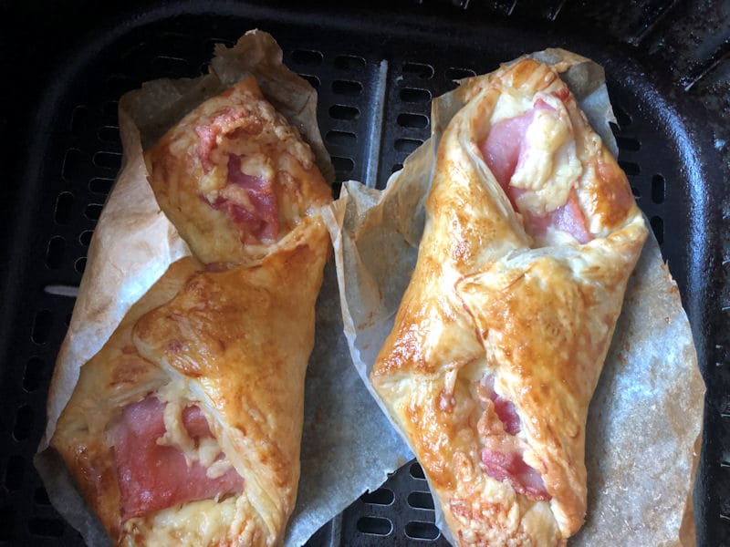 Cooked golden puff pastry bacon turnovers in air fryer on top of parchment