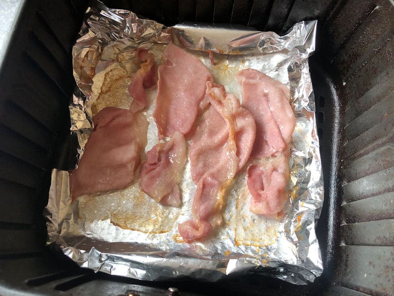 Four back bacon rashers cooking on foil in air fryer basket