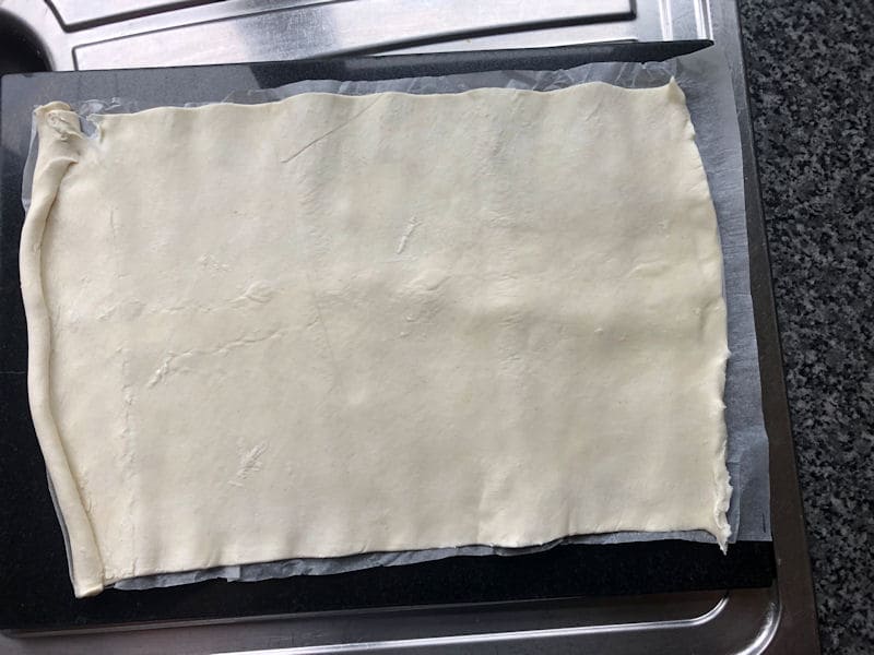 Unraveled puff pastry sheet on chopping board