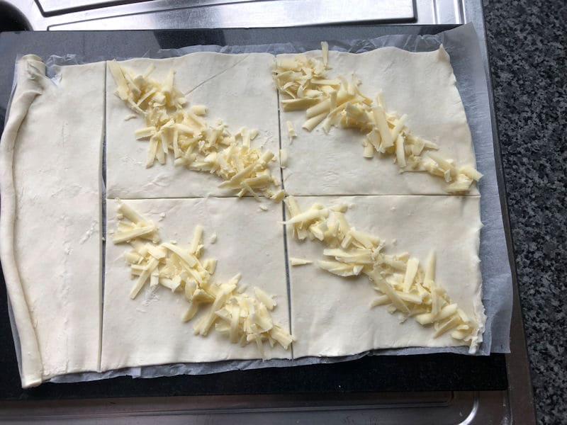 Line of grated cheese from corner to corner on small pastry squares