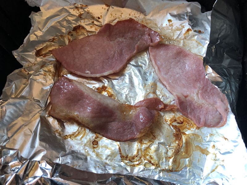 Bacon rashers air frying on sheet of foil lining inside basket