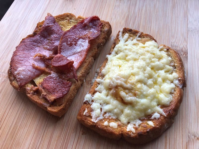 Cooked two toasted bread with melted cheese and egg, other slice has bacon