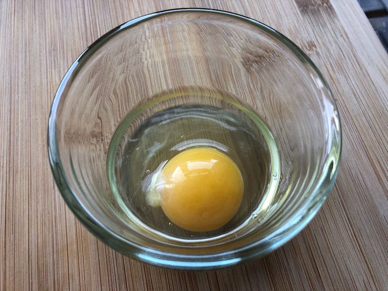 Single raw egg cracked open into glass ramekin