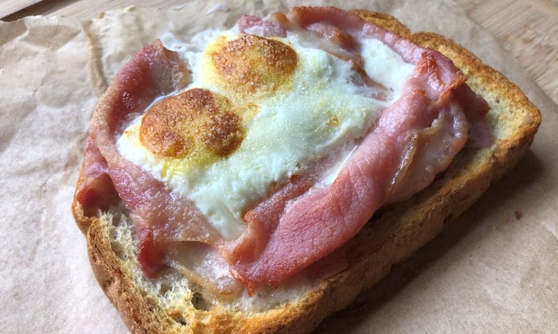 Bacon and double egg open face toast served on parchment paper