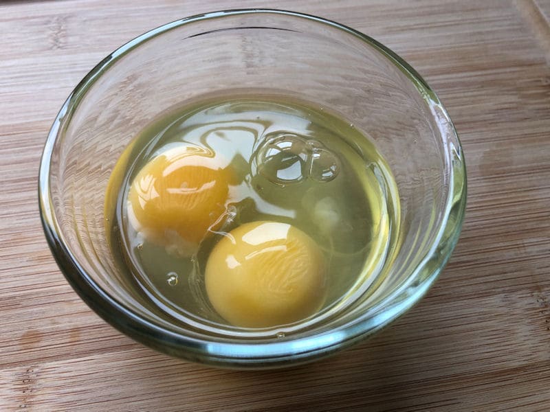 Raw eggs cracked into small glass ramekin dish