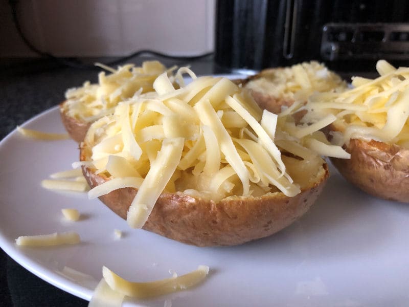 Four jacket potato halves with grated cheese sitting on dinner plate