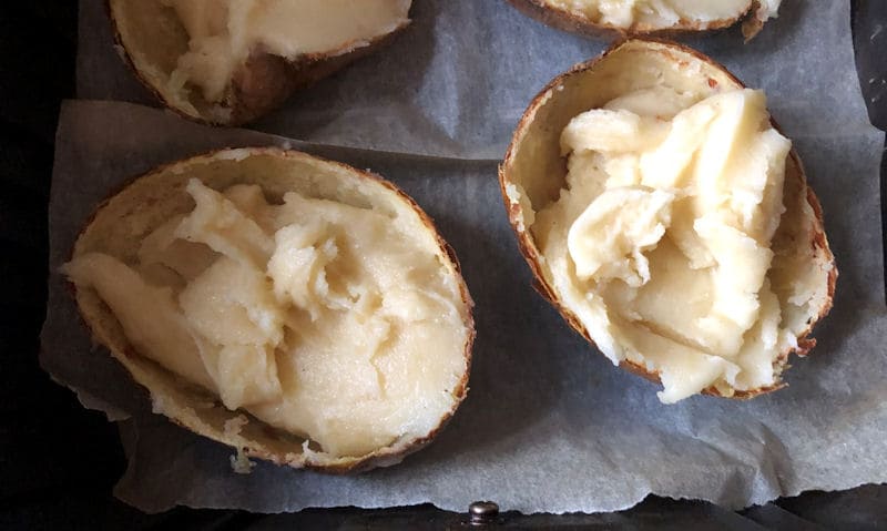 Jacket potato halves sitting on parchment paper in air fryer