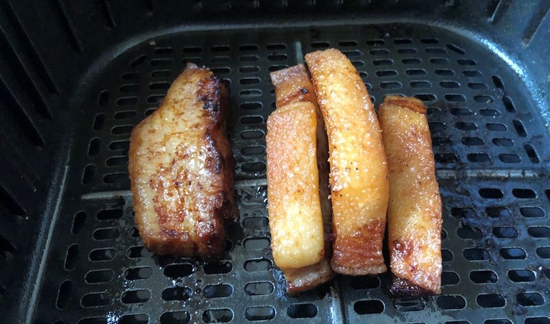 Four juicy pork belly slices sitting in air fryer basket