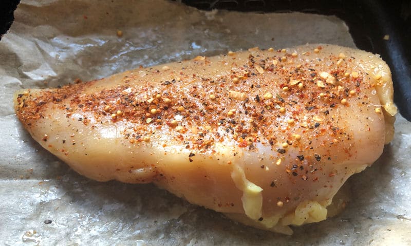 Raw, seasoned chicken breast on baking paper in air fryer