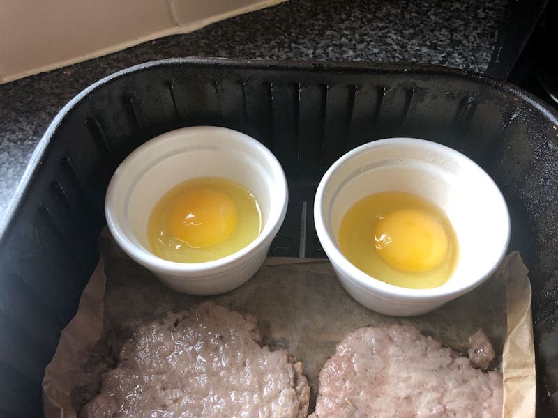 Focus on raw eggs inside two ceramic ramekins inside air fryer