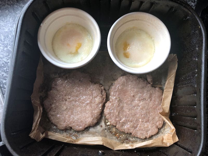 Fully cooked sausage patties and eggs in ramekins, inside air fryer