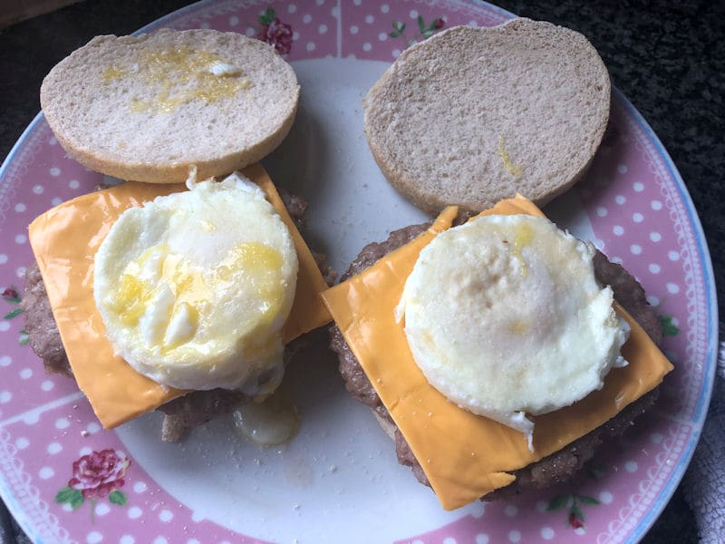 Layer of sausage patties, cheese slice and egg on English muffins