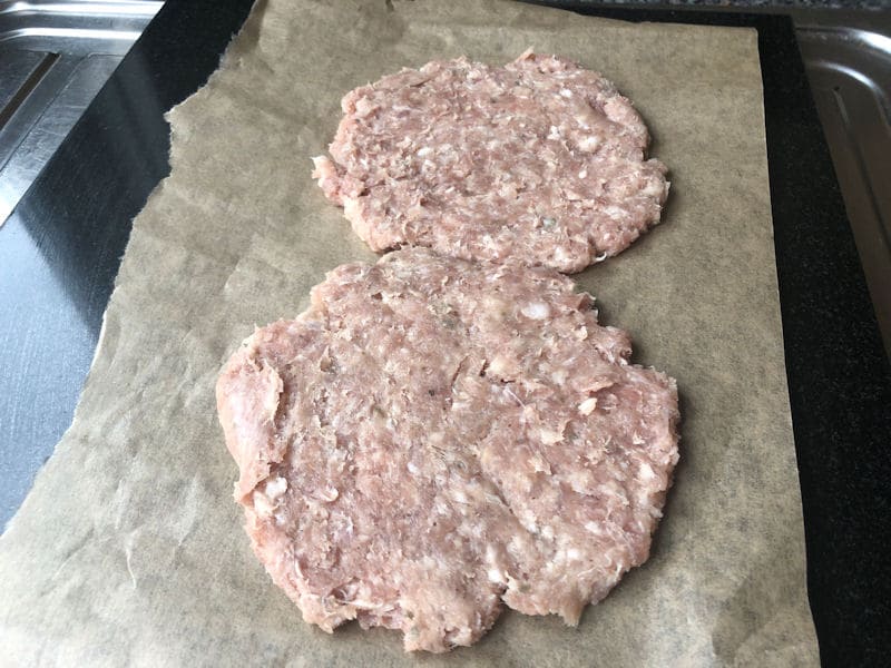 Pair of sausage patties flattened on parchment paper