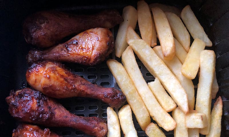 Five BBQ chicken drumsticks with chips in air fryer basket