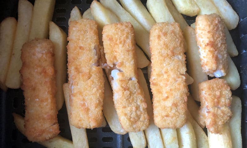 Fish fingers positioned on top of chips inside air fryer