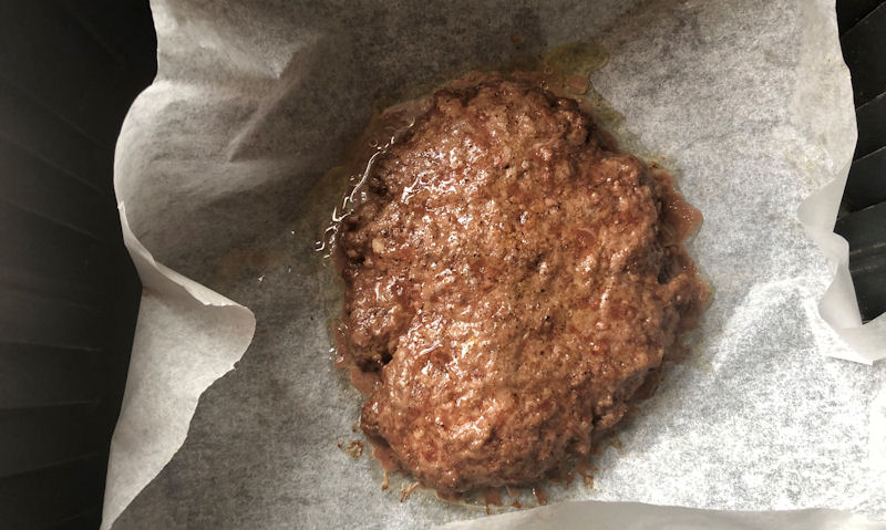 Hamburger patty centered in air fryer basket sitting on parchment paper