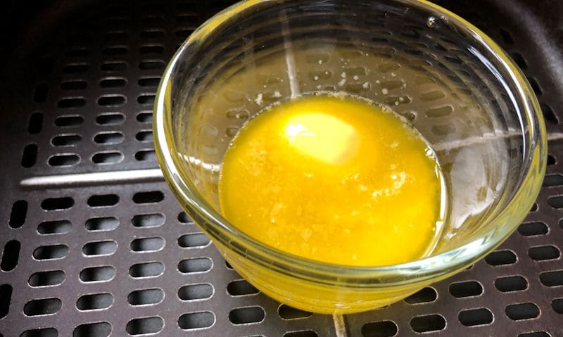 Glass ramekin of melted butter inside air fryer basket