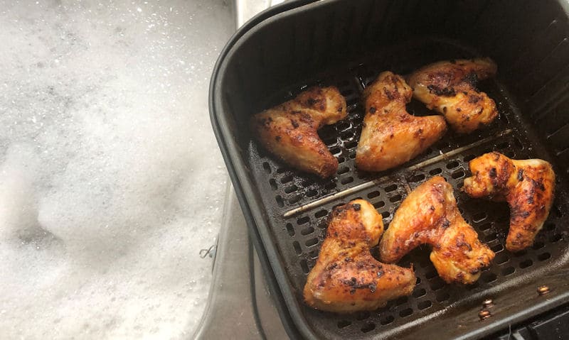 Chicken wing-filled air fryer basket next to soapy sink