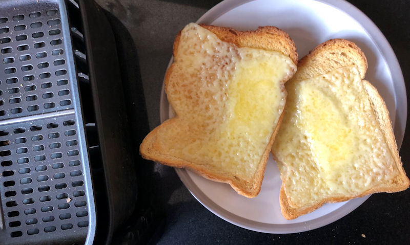 Slices of cheese on toast on plate sitting next to empty air fryer basket