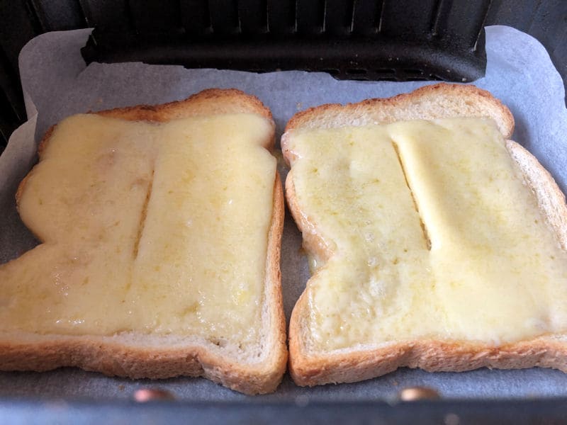 Melted cheese on toast inside parchment paper-lined air fryer basket