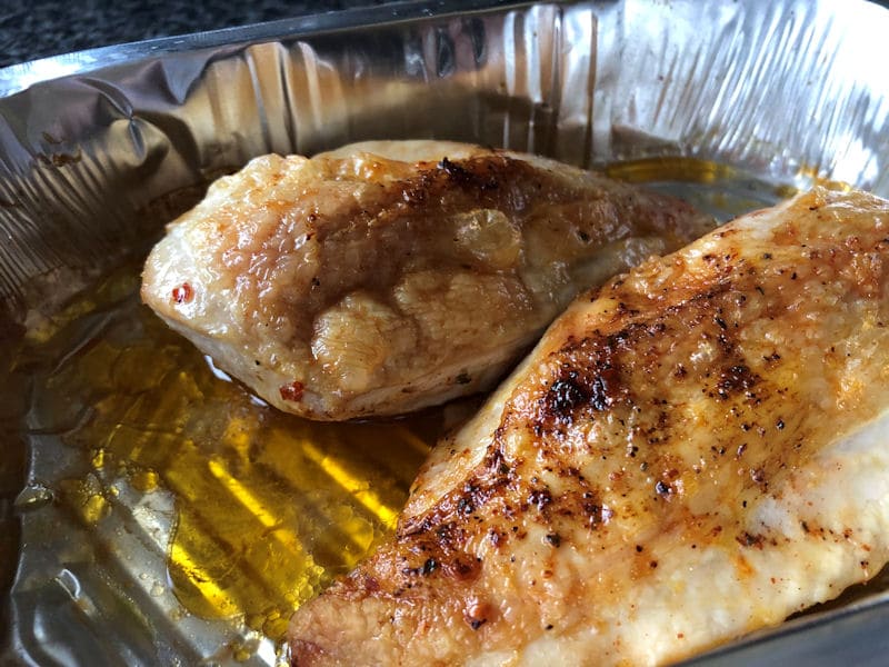 Air fried chicken breasts sat in foil tray surrounded in juices