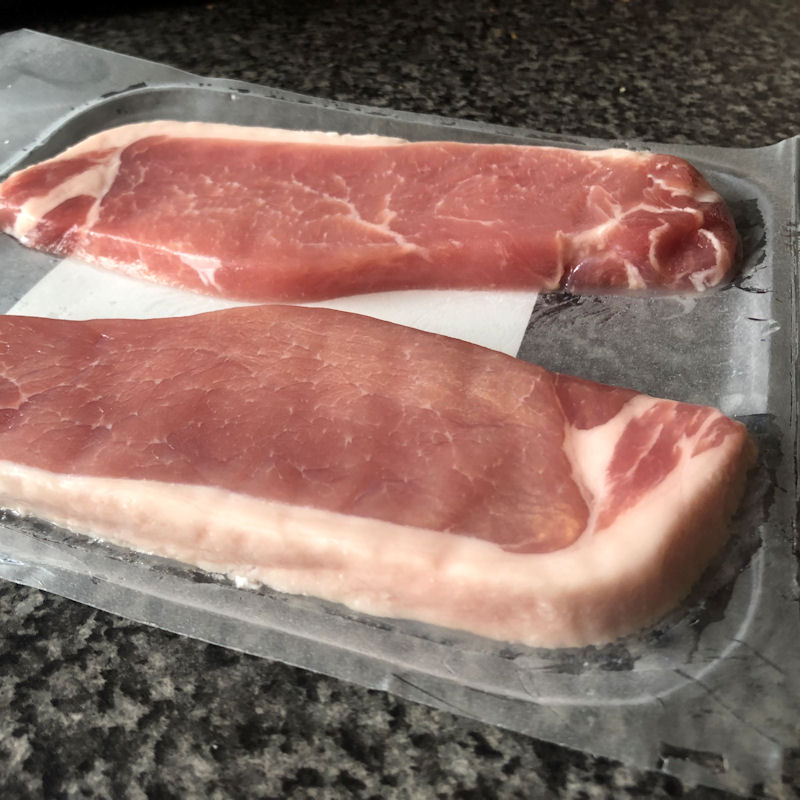 Close look at thickness of bacon chops laid out in open plastic packaging