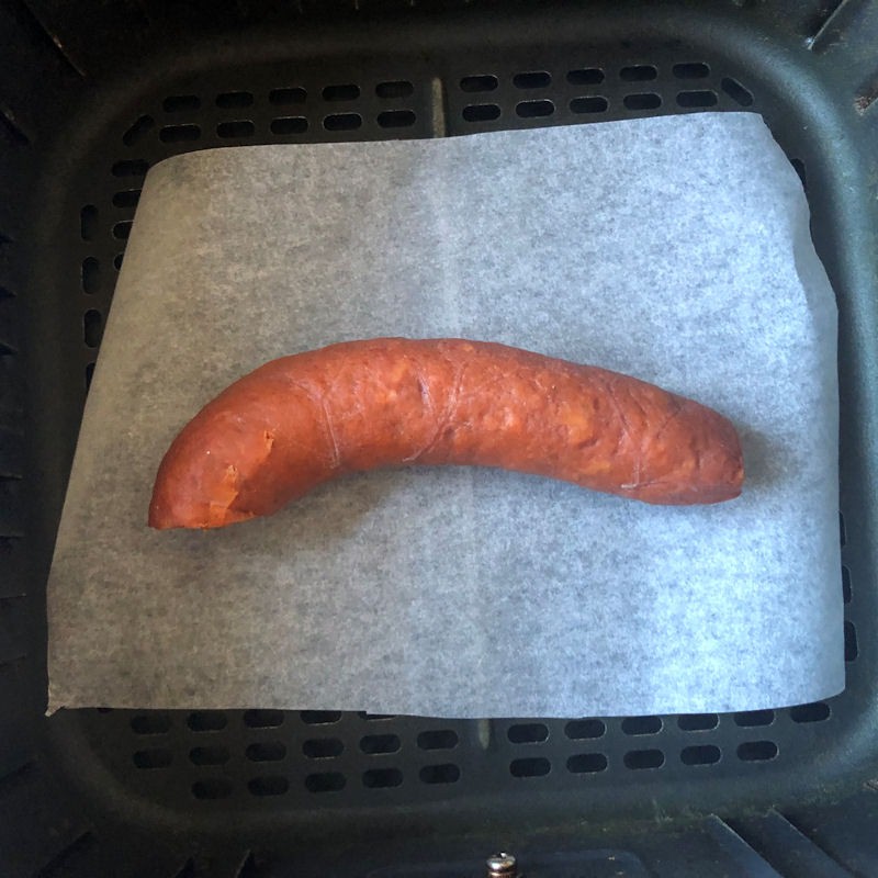 Half of Chorizo ring sat on parchment paper in air fryer basket