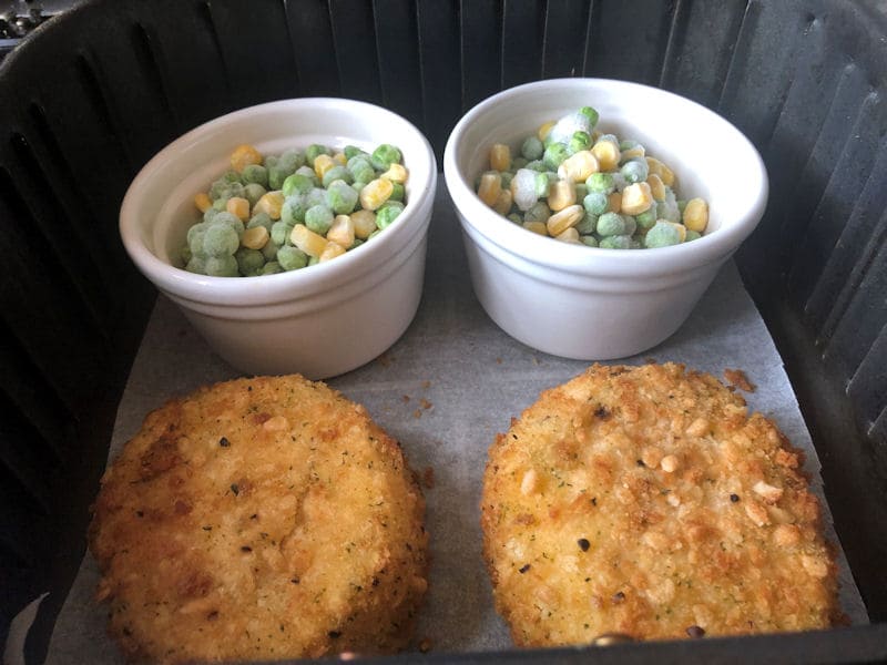 Fish cakes air frying next to 2 mixed vegetable-filled ramekins