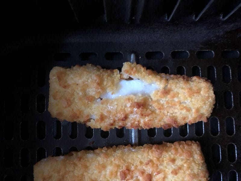 Fish finger sat in air fryer basket with split open breaded coating