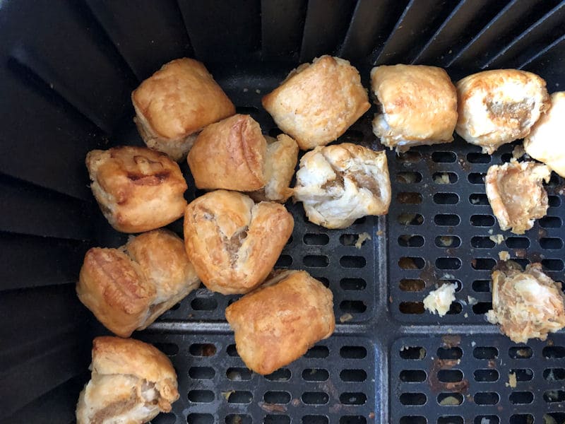 Several fully air fried party sausage rolls piled on side of air fryer basket