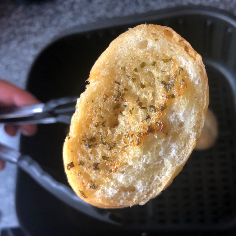 Displaying cooked garlic baguette ends held in tongs