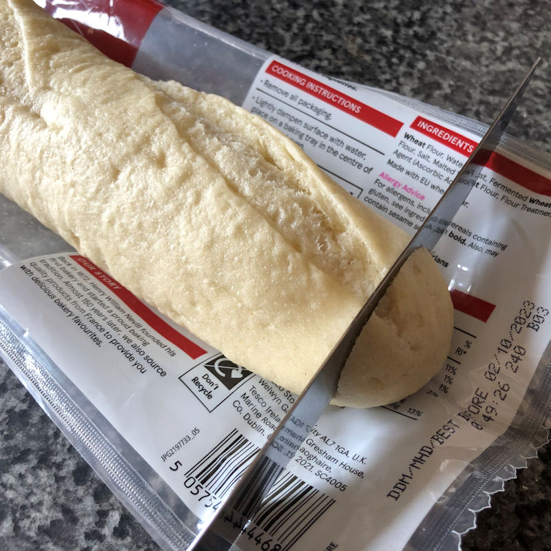 Cutting off end of part baked baguette with knife on top of packaging