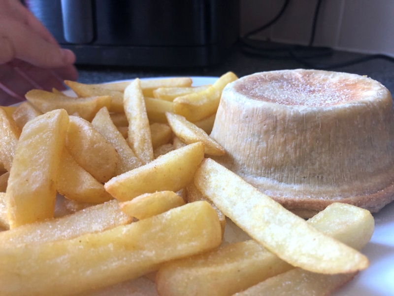 Dinner plate of steak and potato pie with portion of cooked frozen chips