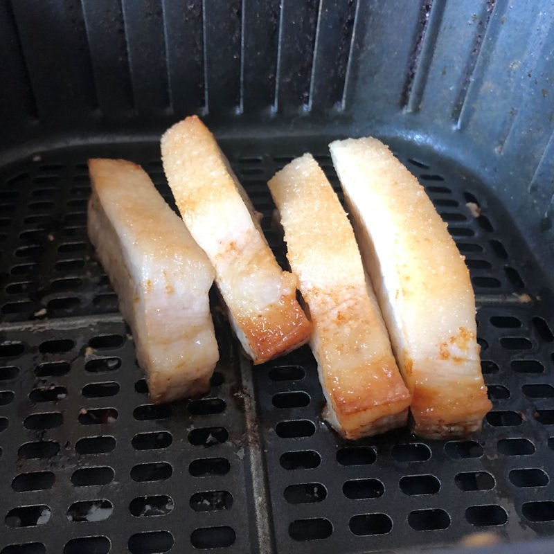 Partially cooked pork belly slices in air fryer basket