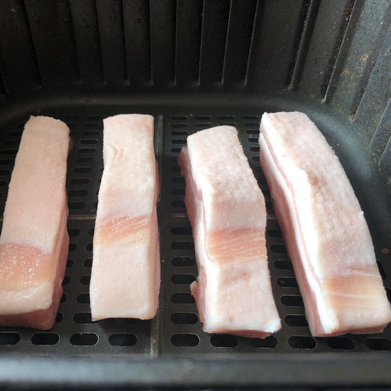 Raw pork belly slices standing side by side in air fryer basket