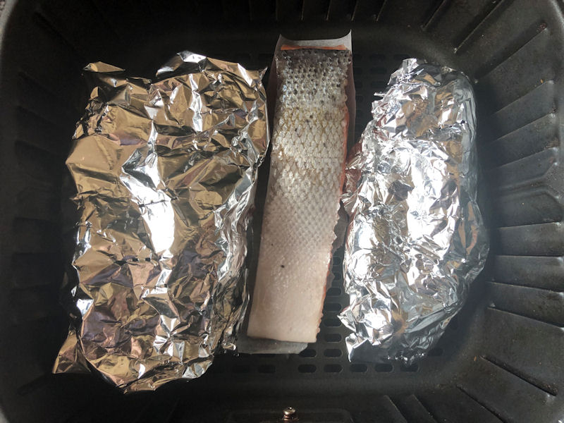 Salmon fillet squeezed in between vegetable-filled foil parcels in air fryer