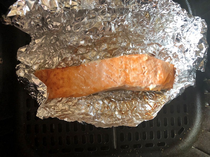 Salmon fillet sat in open foil wrap inside air fryer basket