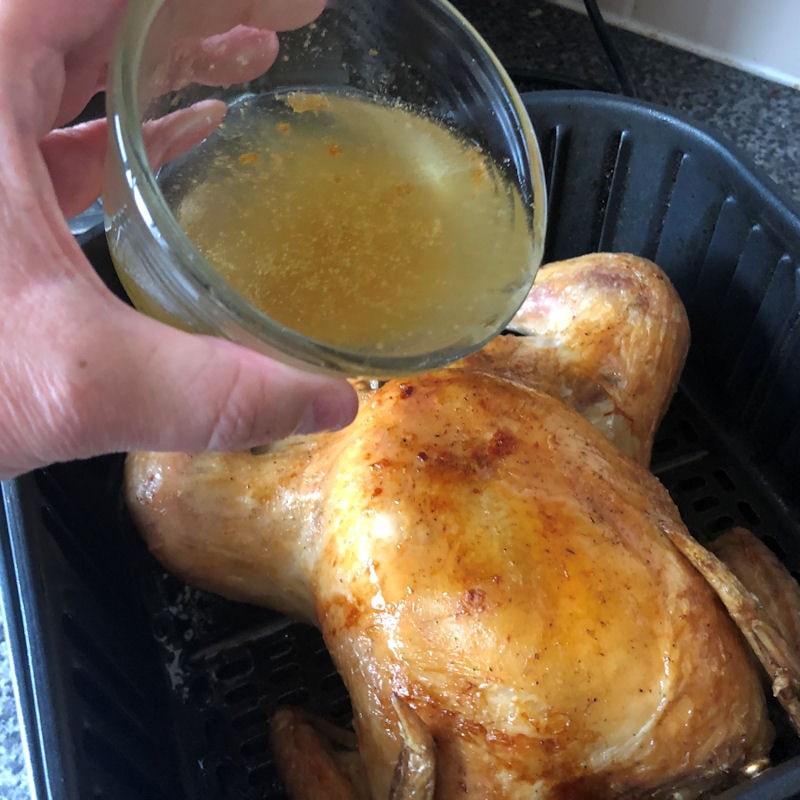 Pouring basting juices out of glass bowl onto chicken in air fryer basket