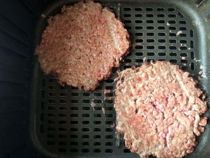 Pair of partially air fried homemade beef patties in air fryer basket