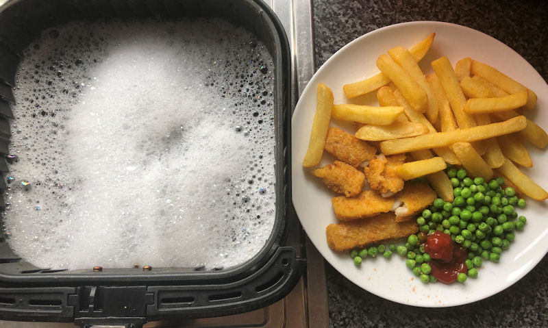 Plate of fish fingers and fries next to air fryer basket full of soapy water