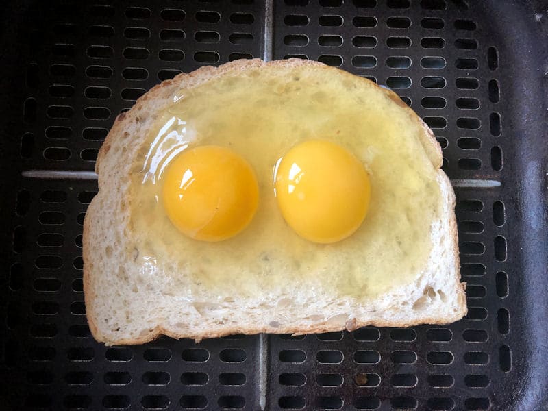 Raw eggs poured into imprint of slice of bread, sat in air fryer basket