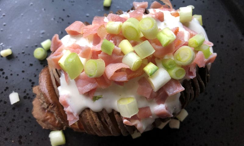 Plated Hasselback potato topped with sour cream, bacon, spring onion