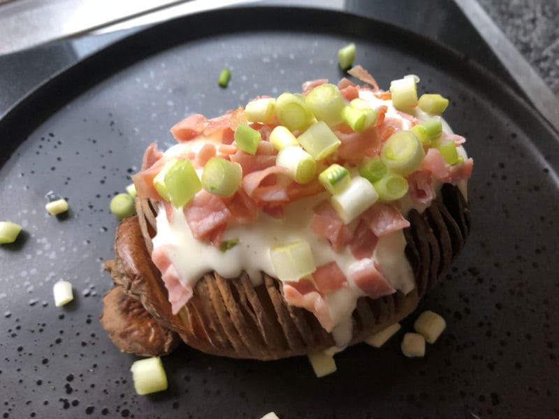 Spring onion sprinkled on top of sour cream dressing on Hasselback potato