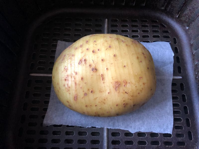 Hasselback potato sat on parchment inside air fryer